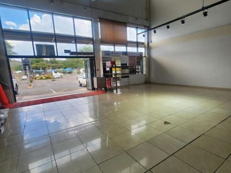 Spacious commercial open-plan unit featuring high ceilings, exposed steel trusses, large glass storefront windows, and polished ceramic tile flooring.