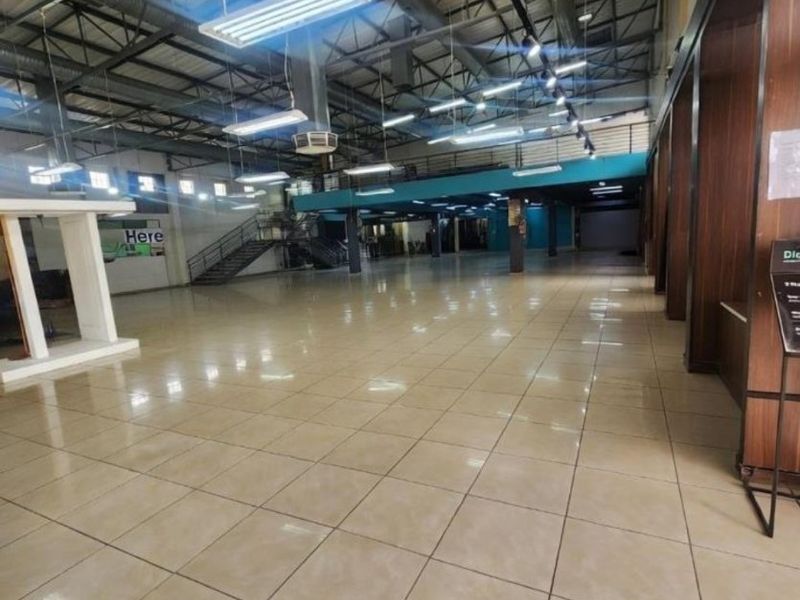 Spacious open-plan commercial interior featuring high exposed industrial ceilings, tiled flooring, and a mezzanine level with metal staircase access.