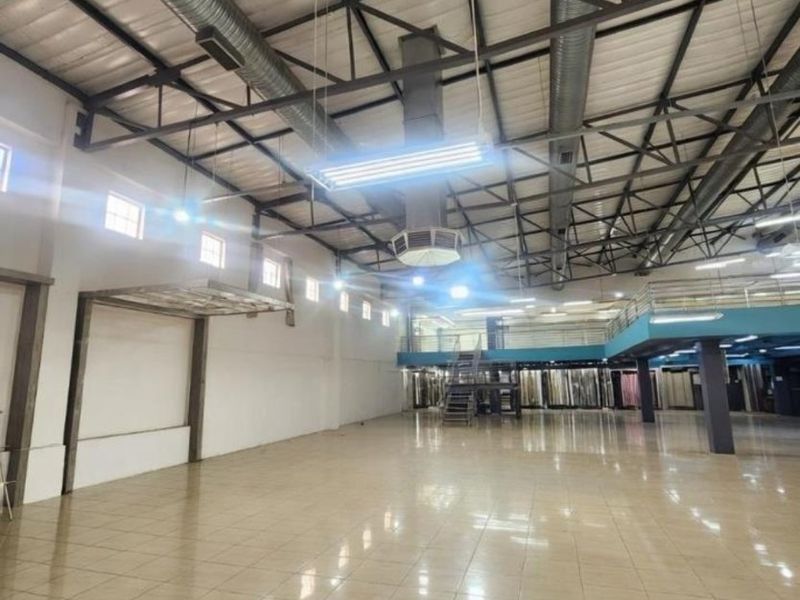 Spacious open-plan commercial warehouse area featuring high exposed ceilings, industrial ducting, tiled flooring, and a mezzanine level with metal staircase access.