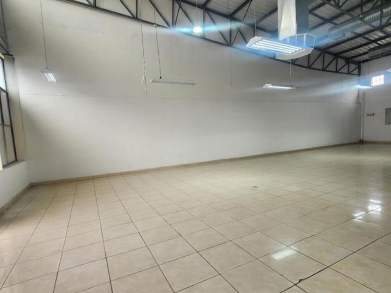 Spacious open-plan commercial area featuring high ceilings with exposed steel trusses, industrial HVAC ducting, and durable ceramic tile flooring.