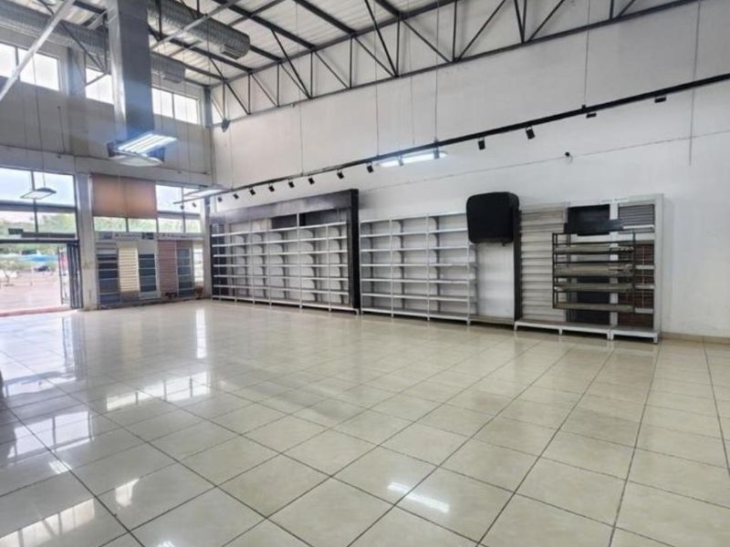 Spacious commercial open-plan area featuring high ceilings with exposed ductwork, tiled flooring, and integrated metal shelving units suitable for retail or showroom use.