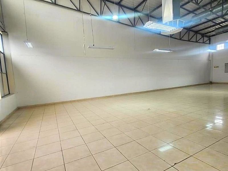 Spacious open-plan commercial area featuring high ceilings with exposed steel trusses, ducted HVAC, and durable ceramic tile flooring, suitable for various business applications.