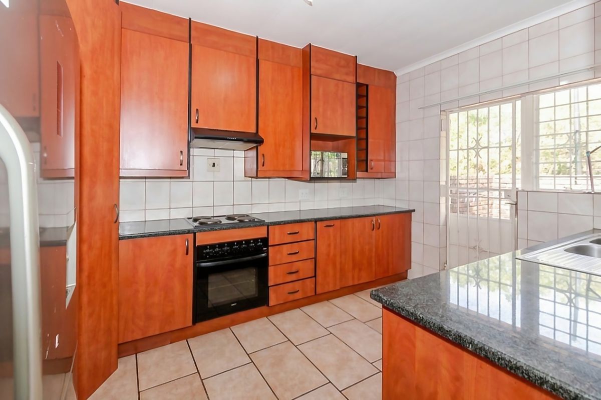 A functional kitchen featuring warm-toned wooden cabinetry, granite countertops, a built-in oven and hob, and direct access to an outdoor area via a security gate.
