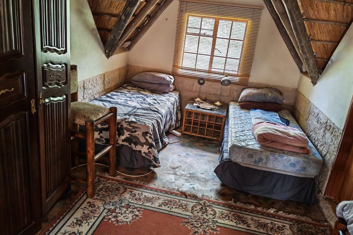 A rustic bedroom featuring exposed thatch roofing, timber rafters, and stone masonry walls, offering a unique farm-style aesthetic with potential for cosmetic updates.