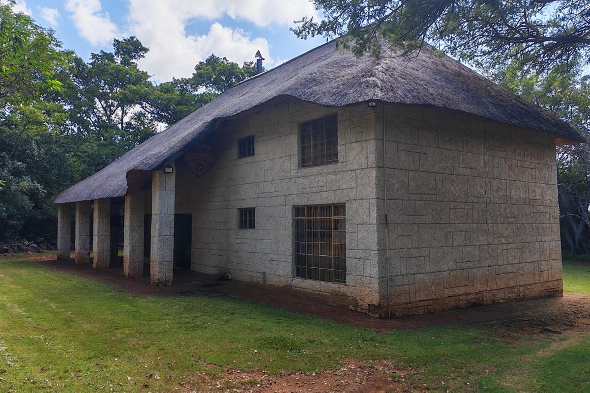 Rear view of a two-story farm house featuring traditional thatch roofing, stone masonry walls, and a covered patio area set within a garden.