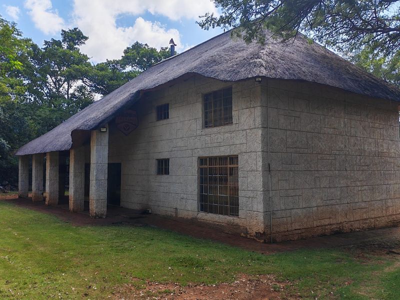 Rear view of a two-story farm house featuring traditional thatch roofing, stone masonry walls, and a covered patio area set within a garden.