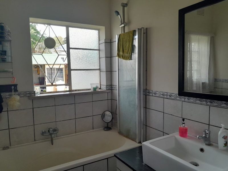 A functional bathroom featuring a built-in bathtub, shower attachment, and a vanity basin with tiled wall finishes.