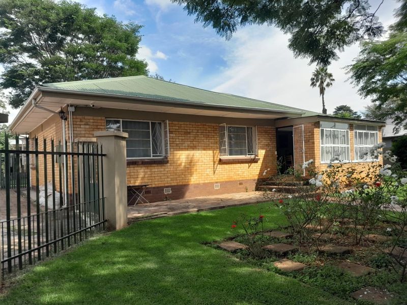 A classic single-story face-brick house featuring a metal roof, security window bars, and a well-maintained front garden with a paved walkway.