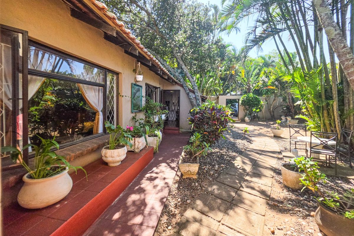 A rear exterior view featuring a tiled patio area, paved garden walkway, and established landscaping along the side of the house.