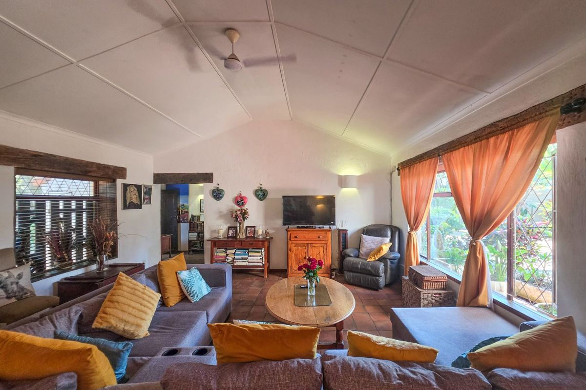 Spacious living room featuring a vaulted ceiling with a fan, terracotta tiled flooring, and large windows providing natural light and garden views.