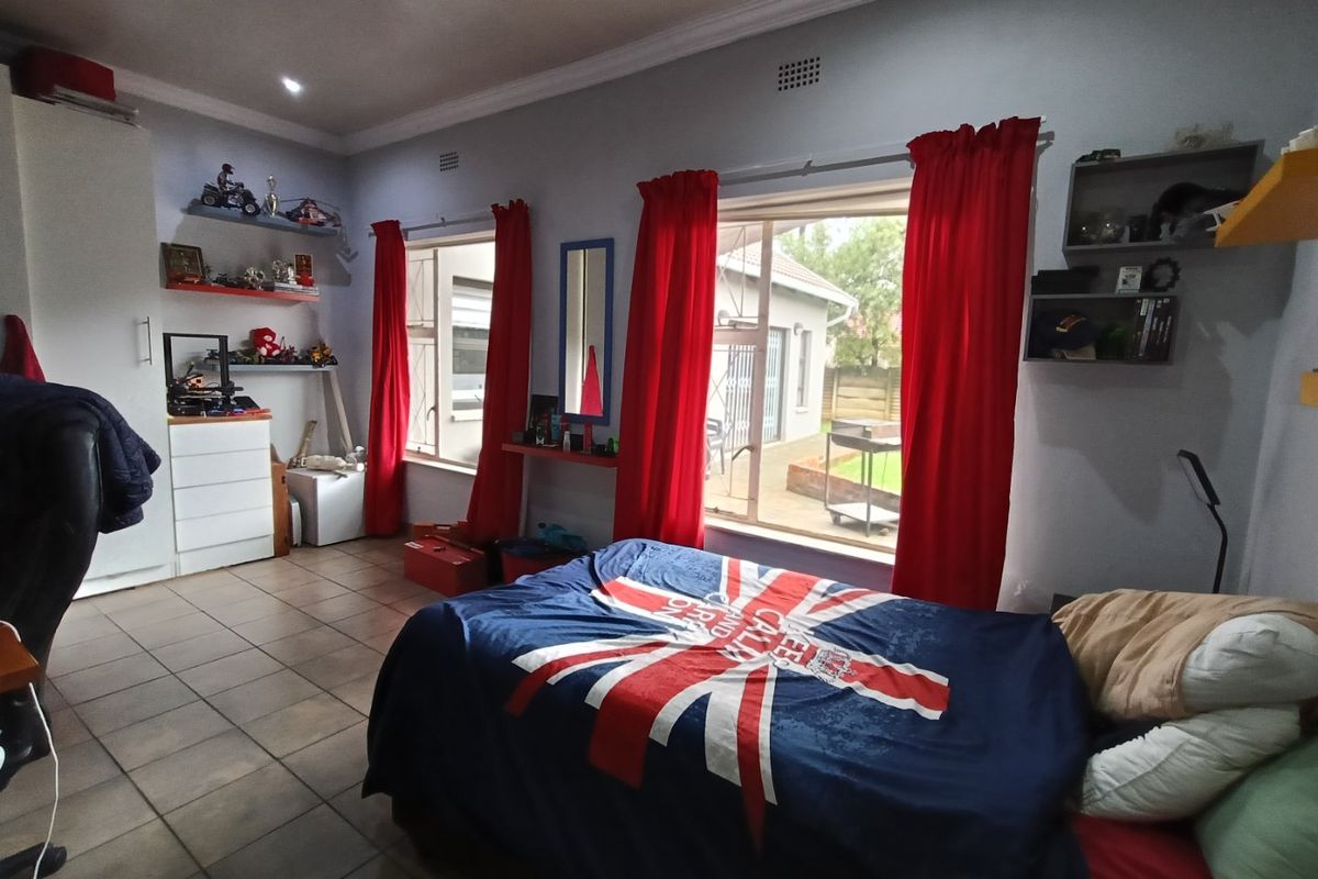 A bedroom featuring tiled flooring, built-in cupboards, and large windows with views of the rear garden area.