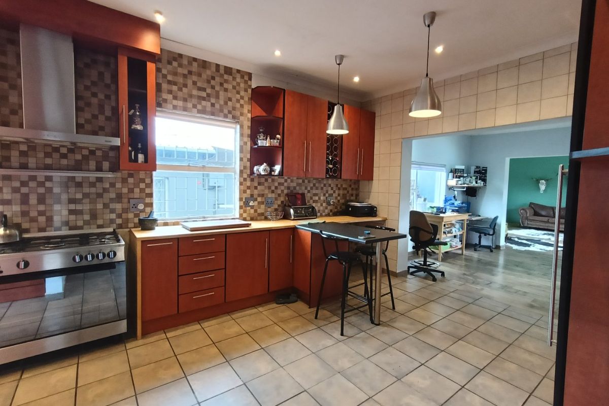 A functional kitchen featuring wooden cabinetry, tiled backsplash, gas stove with extractor, and tiled flooring, with an adjacent open-plan living area.