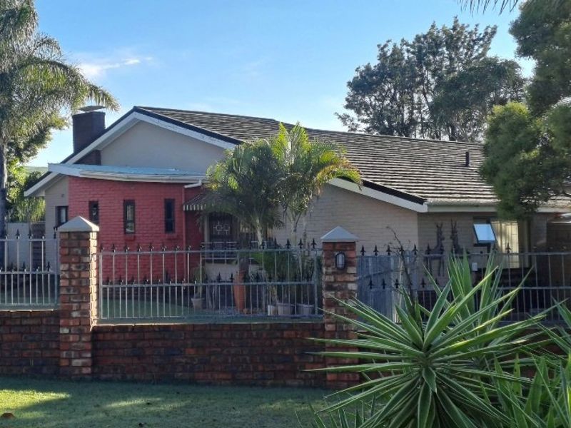 Front elevation of a single-story house featuring a brick perimeter wall, metal security fencing, and a tiled roof with a prominent chimney.