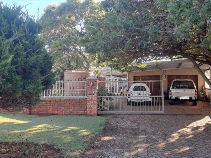 Front exterior view of the property featuring a brick boundary wall, metal gate, paved driveway, and covered carport area.