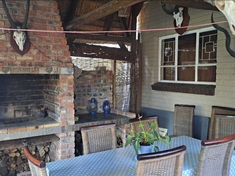 Covered outdoor patio area featuring a built-in brick braai, rustic thatched roofing, and exposed timber beams, ideal for outdoor entertaining.