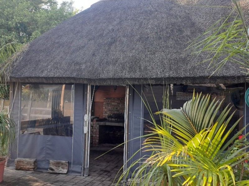Outdoor thatched lapa area featuring a built-in brick braai, paved flooring, and protective roll-up canvas blinds for all-weather entertainment.