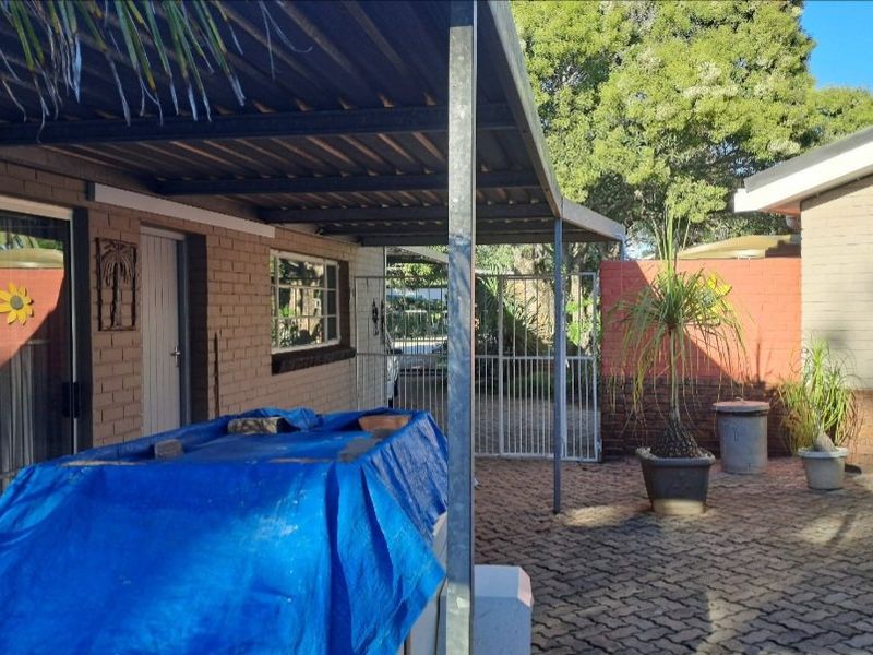 A covered outdoor patio area featuring brick paving, a corrugated metal roof, and direct access to the home via a sliding glass door.