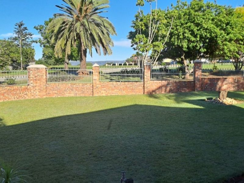 A well-maintained garden featuring a brick boundary wall with integrated metal fencing and mature trees.