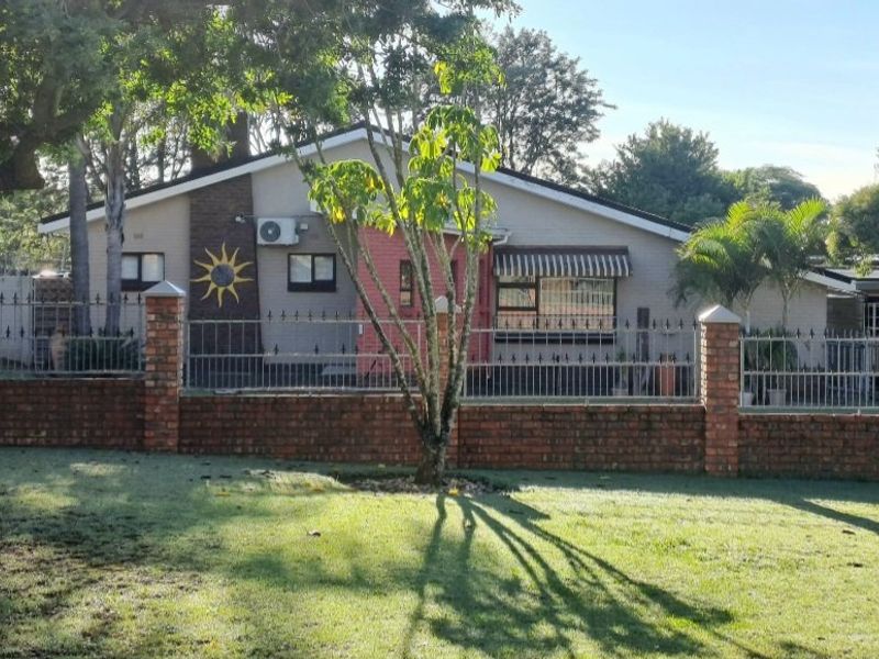 Front view of a single-story house featuring a brick boundary wall, metal security fencing, and an established garden.