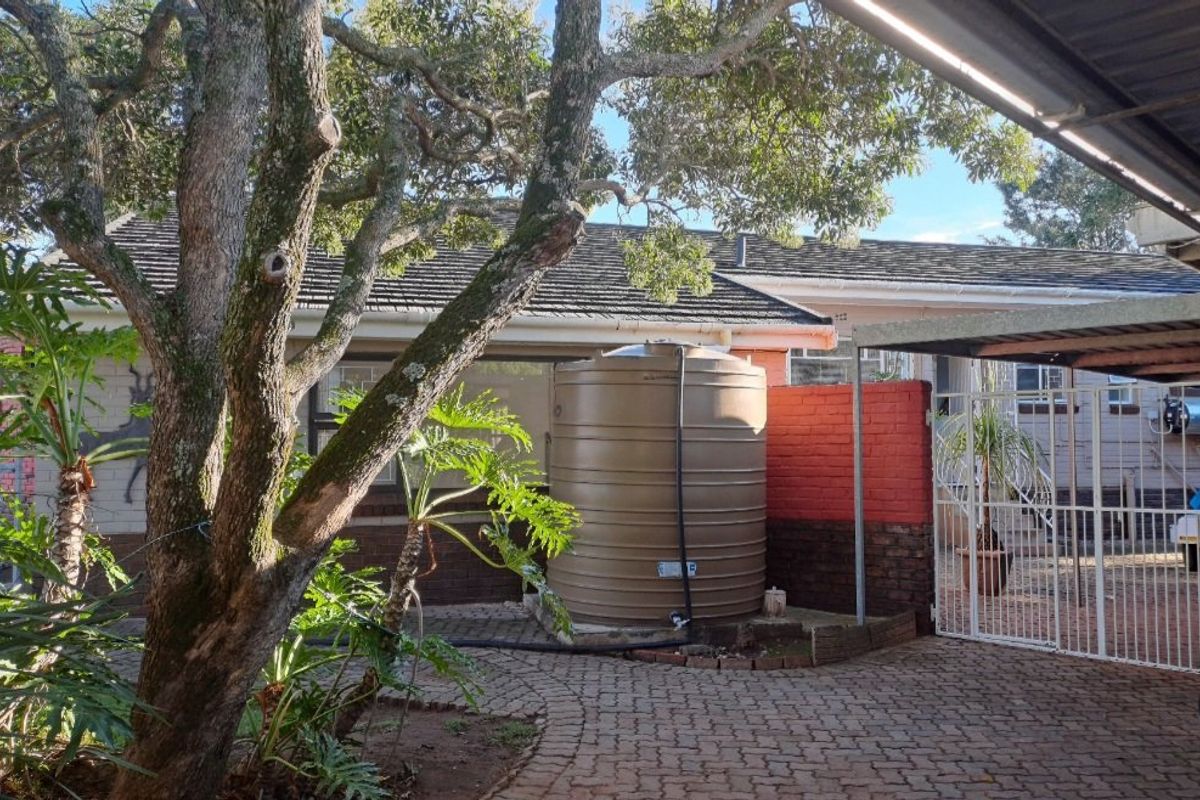 Rear exterior view featuring a paved courtyard, a large water storage tank, and a covered carport area.