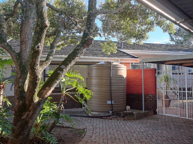 Rear exterior view featuring a paved courtyard, a large water storage tank, and a covered carport area.