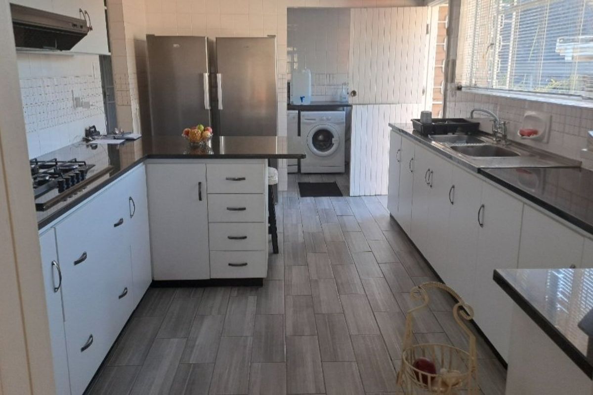 Functional kitchen featuring white cabinetry, granite countertops, gas hob, extractor fan, and tiled flooring, with an adjacent laundry area visible.