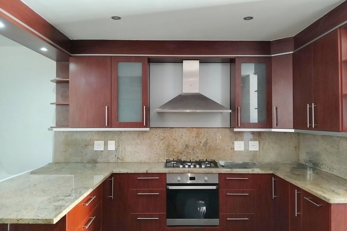 A well-maintained kitchen featuring dark wood cabinetry, granite countertops, a built-in oven, gas hob, and a stainless steel extractor fan.