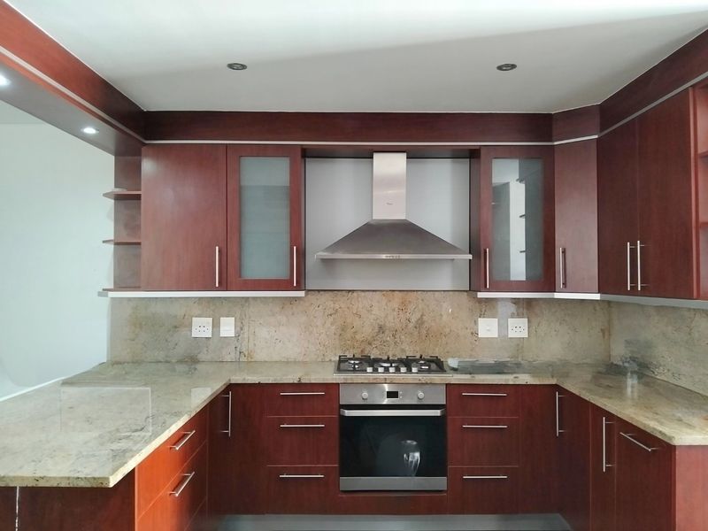 A well-maintained kitchen featuring dark wood cabinetry, granite countertops, a built-in oven, gas hob, and a stainless steel extractor fan.