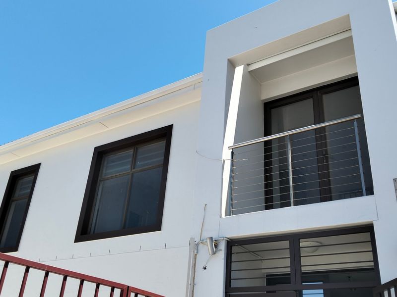 Exterior view of a modern two-story residential facade featuring a balcony with stainless steel balustrades and secure metal gate access.