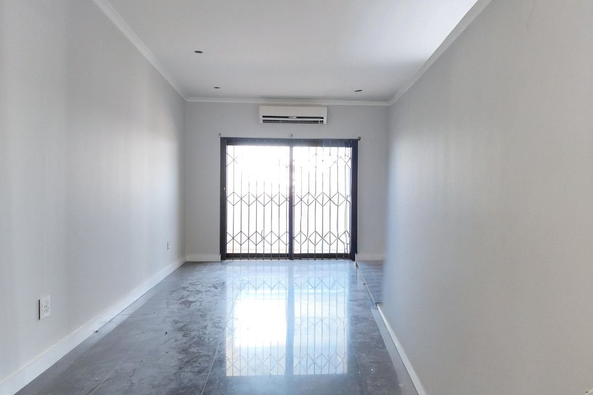 An empty living room featuring tiled flooring, recessed lighting, a wall-mounted air conditioning unit, and a sliding glass door with a security gate.