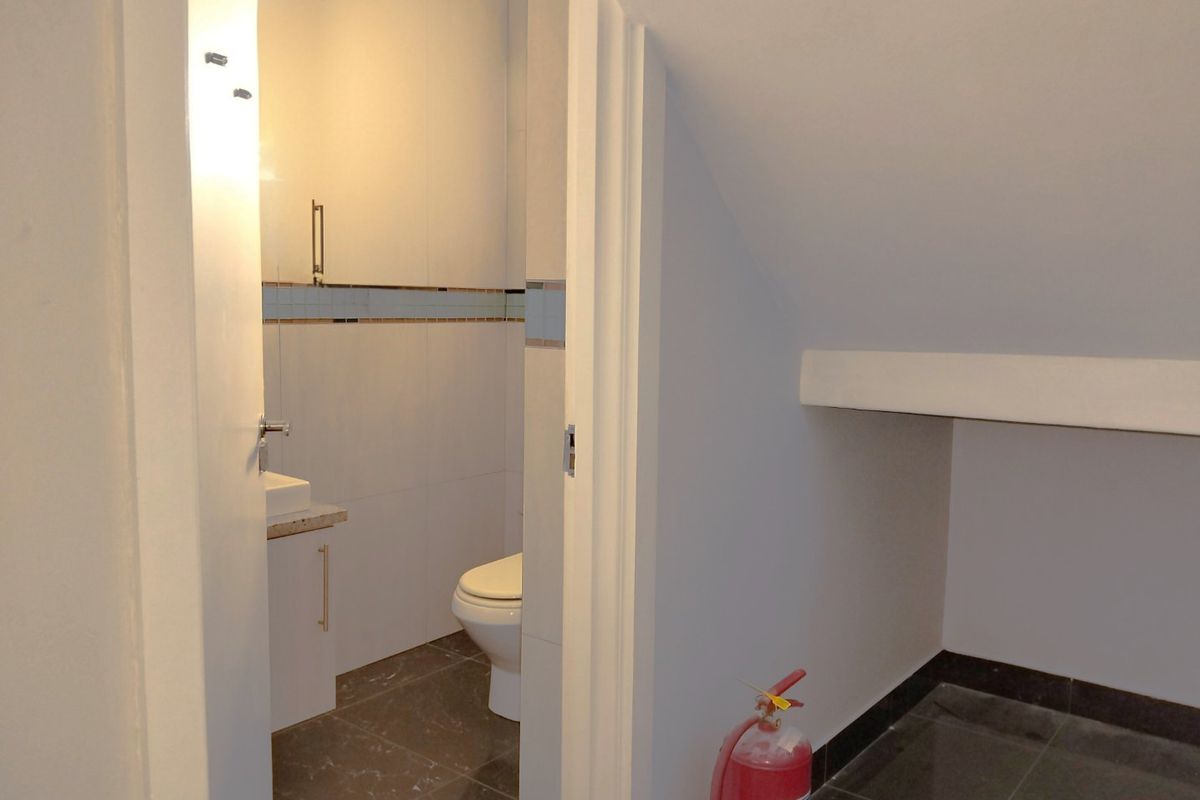 A compact bathroom featuring a modern vanity, basin, and toilet with neutral wall and floor tiling, situated under a sloped ceiling.