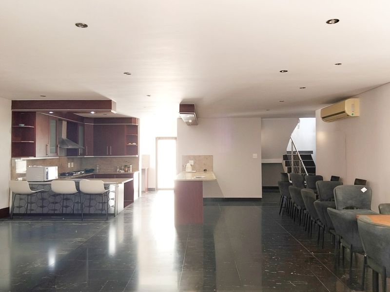 Spacious open-plan living area featuring a modern kitchen with built-in cabinetry, a central island, and polished stone flooring, leading to a staircase.