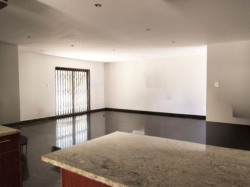 Spacious open-plan living area featuring polished tiled floors, recessed lighting, and a granite-topped kitchen island, leading to a secure exterior access point.
