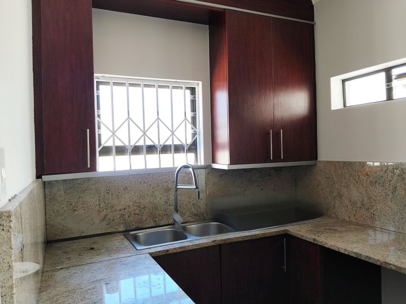 A clean kitchen area featuring dark wood cabinetry, granite countertops, and a double bowl stainless steel sink with a modern mixer tap.