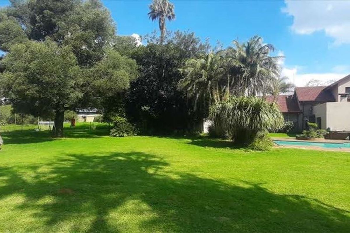 Spacious rear garden featuring a swimming pool, a covered patio area, and a separate thatched roof structure set within a well-maintained lawn.