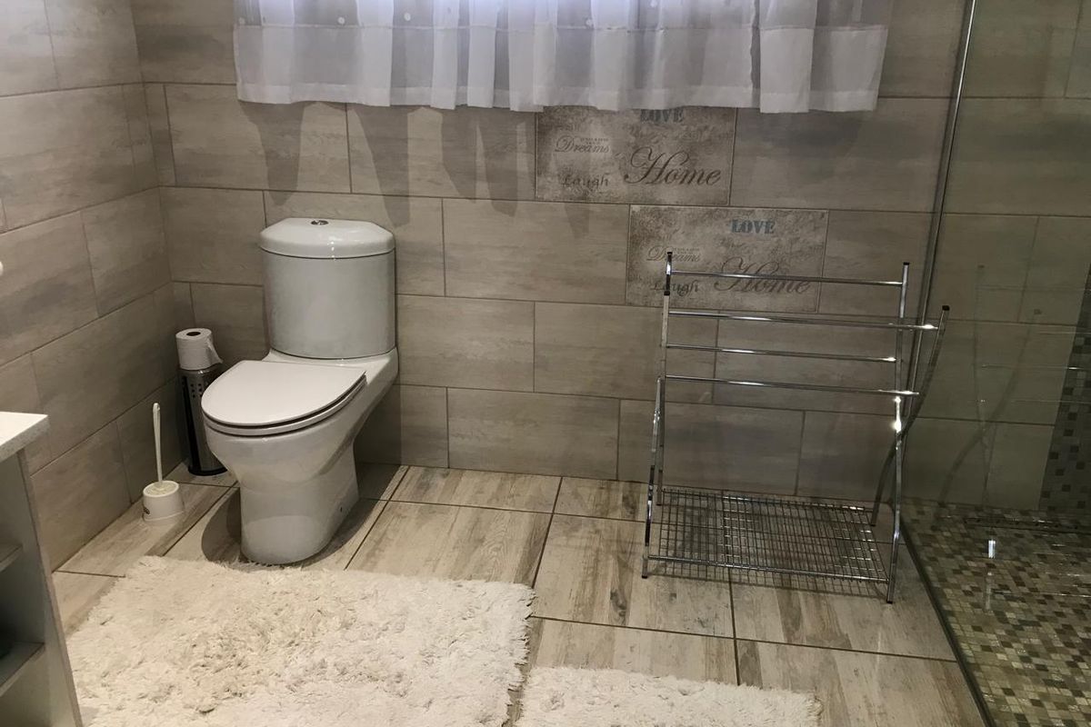 A modern bathroom featuring neutral wood-look floor and wall tiles, a white toilet, and a glass-enclosed shower area.