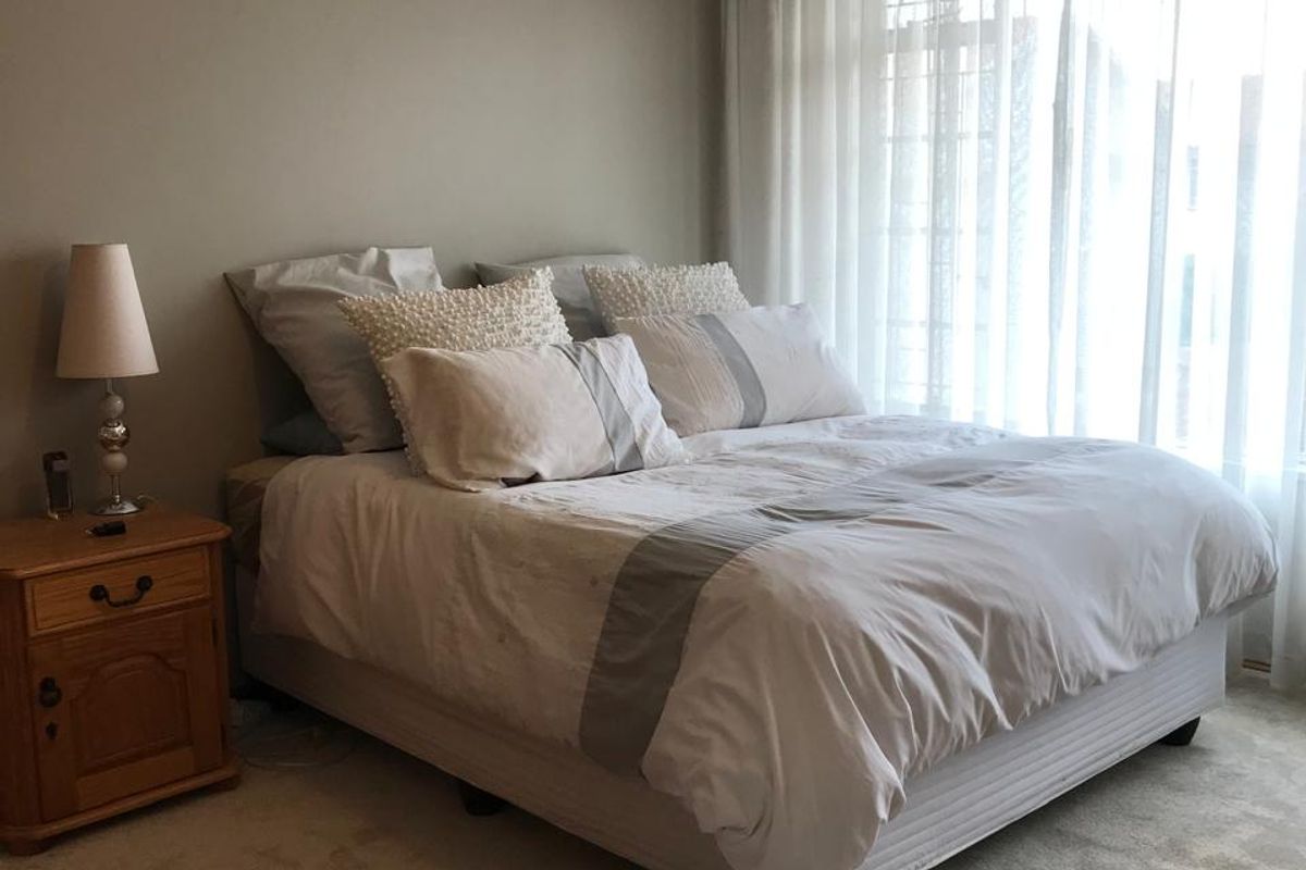 A neutrally painted bedroom featuring carpeted flooring and large windows with sheer curtains, providing ample natural light.