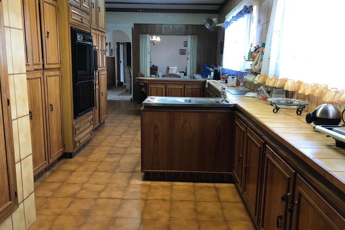 Spacious kitchen featuring extensive built-in wooden cabinetry, double wall oven, tiled countertops, and traditional tiled flooring with exposed ceiling beams.