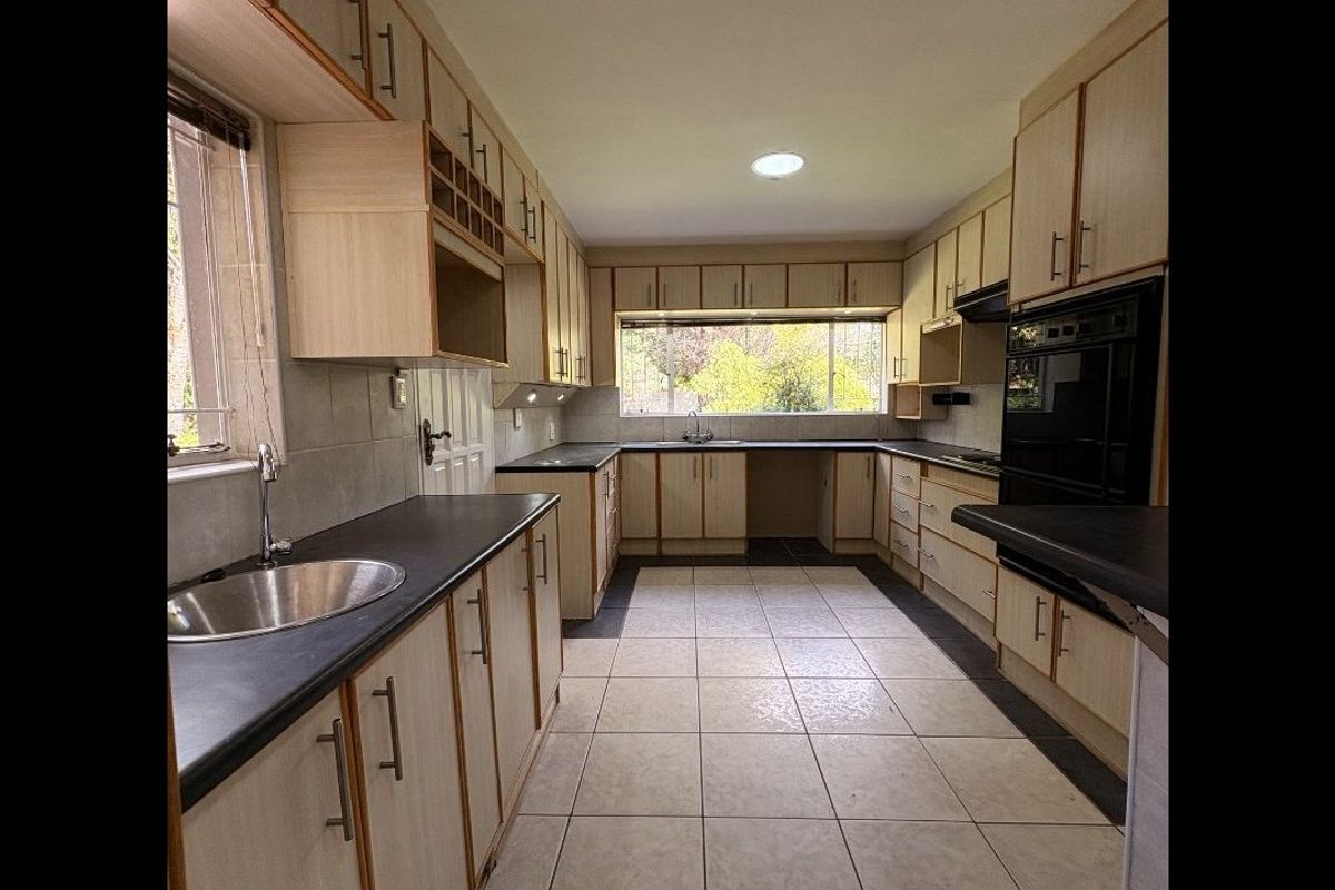 A functional kitchen featuring light wood-toned cabinetry, dark laminate countertops, integrated oven, and tiled flooring with ample natural light.