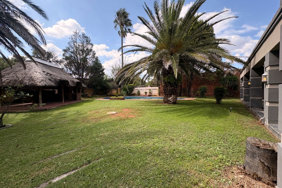 Spacious rear garden featuring a swimming pool, a thatched lapa entertainment area, and established palm trees.