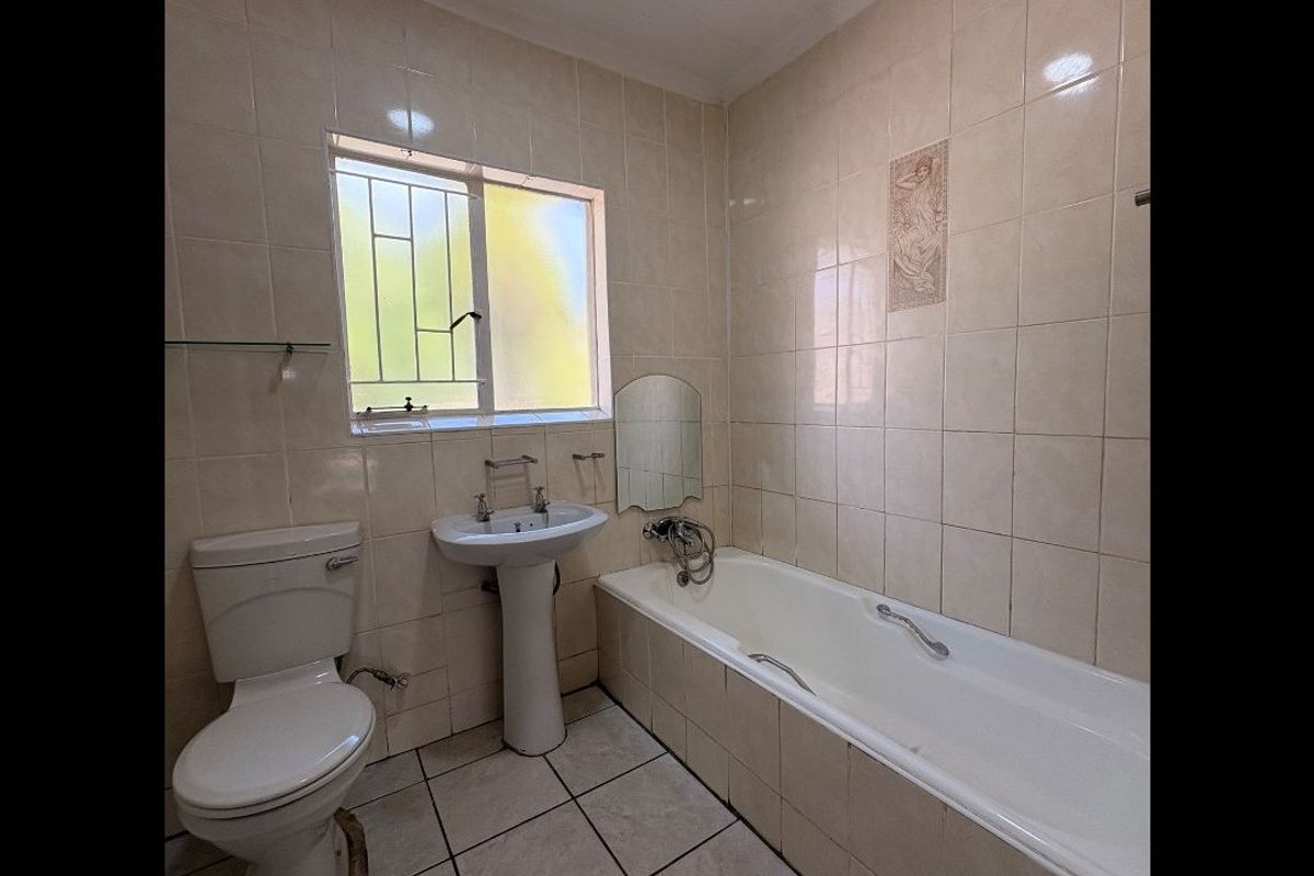 A functional bathroom featuring a pedestal basin, a standard bathtub with shower mixer, and full-height wall tiling.