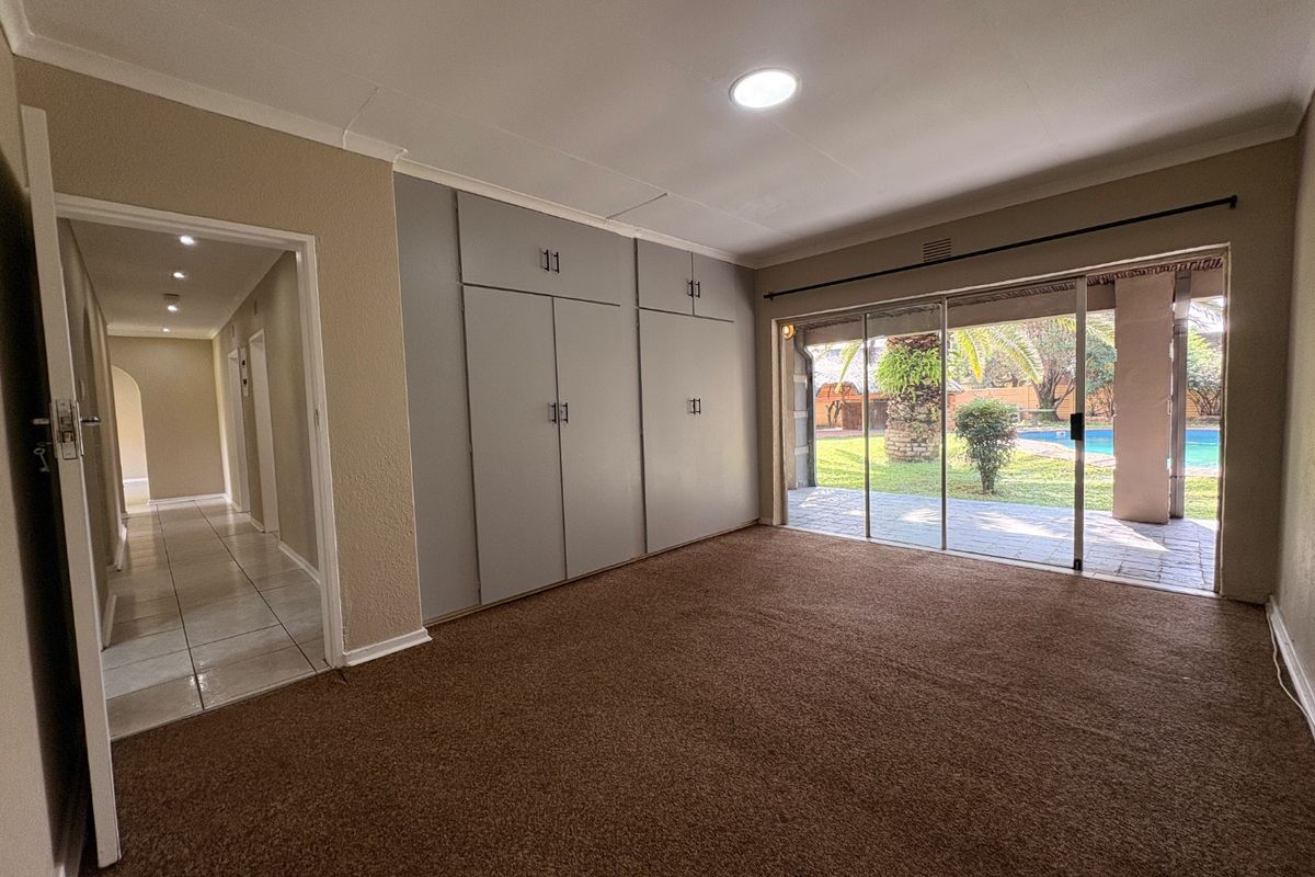 Spacious bedroom featuring built-in cupboards, carpeted flooring, and large sliding glass doors providing direct access to the patio and pool area.