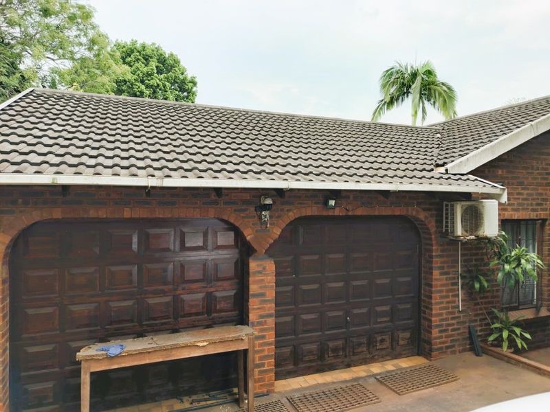 A double garage featuring a brick facade, tiled roof, and dark wood-finish garage doors, with an external air conditioning unit mounted on the side.
