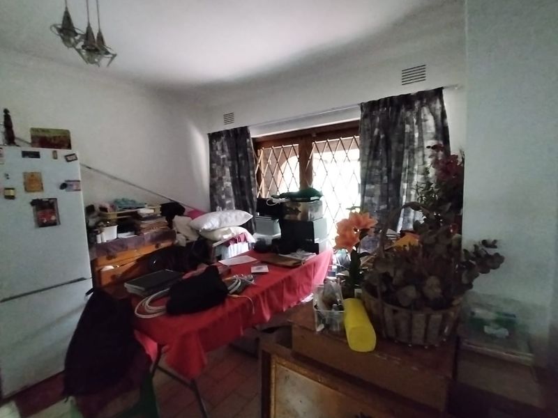 A kitchen area featuring tiled flooring and a ventilation grille, currently cluttered with personal items and furniture.