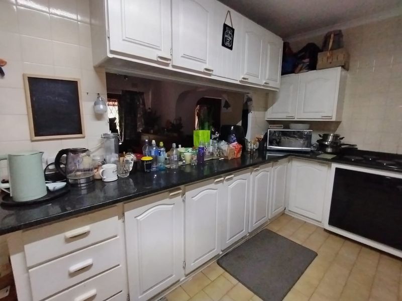 A functional kitchen featuring white cabinetry, dark granite countertops, tiled backsplash, and built-in cooking appliances with a pass-through window to the living area.