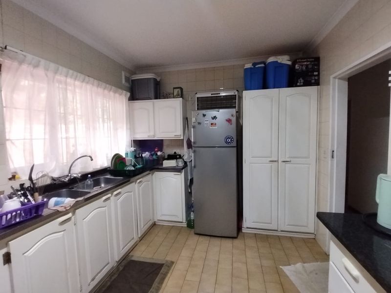 A functional kitchen featuring white built-in cabinetry, a double sink, tiled backsplash, and ample storage space with a dedicated pantry cupboard.