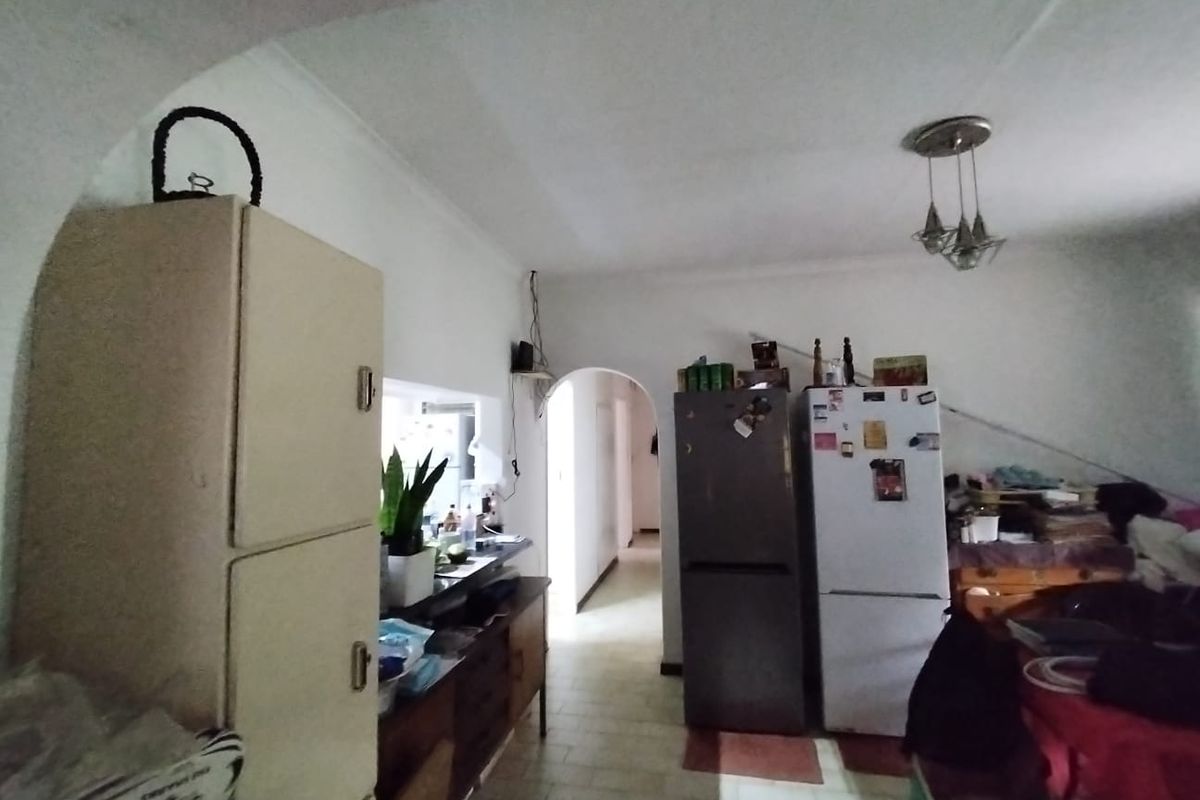 A dated kitchen area featuring original cabinetry, tiled flooring, and a distinctive architectural archway leading to the hallway.
