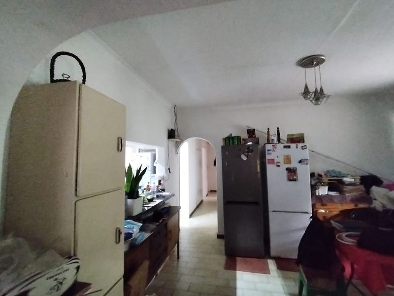 A dated kitchen area featuring original cabinetry, tiled flooring, and a distinctive architectural archway leading to the hallway.