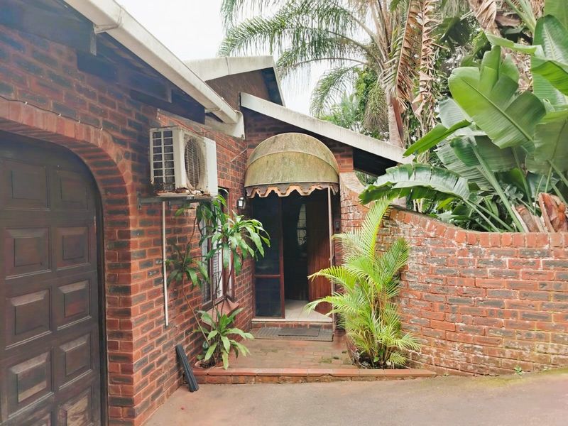 Front entrance of a face brick house featuring an arched doorway, a brick boundary wall, and an external air conditioning unit.
