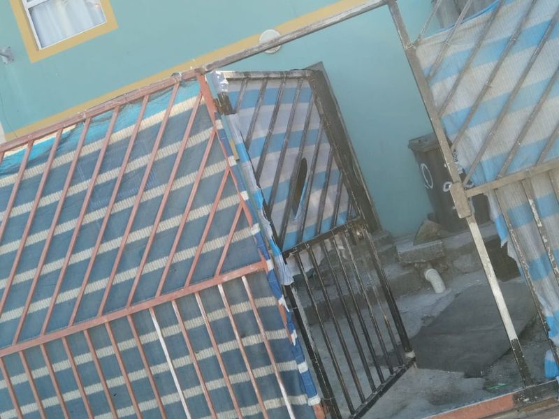 Front exterior view of the property featuring a metal security gate and paved entrance area with visible wear to the structure.